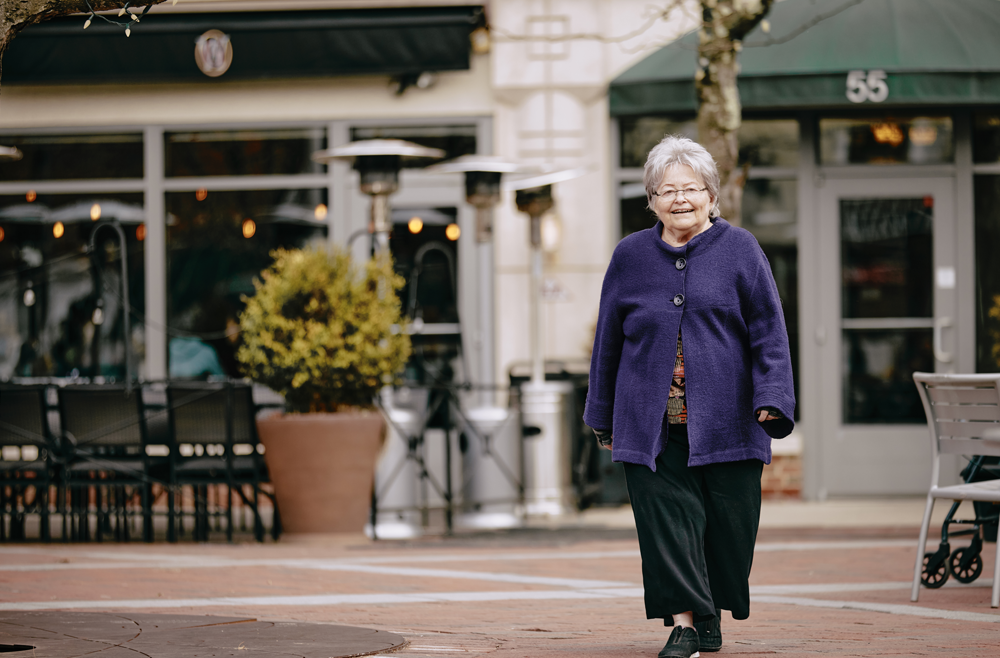 Mimi Reed smiles and walks through a town square with a store in the background